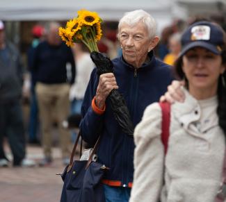 A man holding a bouquet of sunflowers while walking down a street by Joseph Corl courtesy of Unsplash.