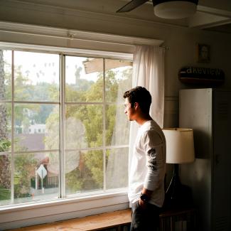 man wearing gray and black crew-neck shirt standing and looking out window by Hamish Duncan courtesy of Unsplash.