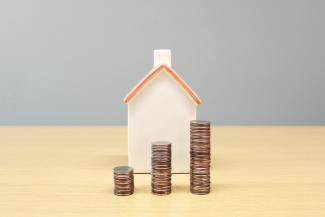 a house and stacks of coins on a table by BuyandRent Homes courtesy of Unsplash.